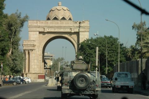 1996 Ford Bronco - A military vehicle drives down a street in front of a large archway, with other cars and a pickup truck also visible.