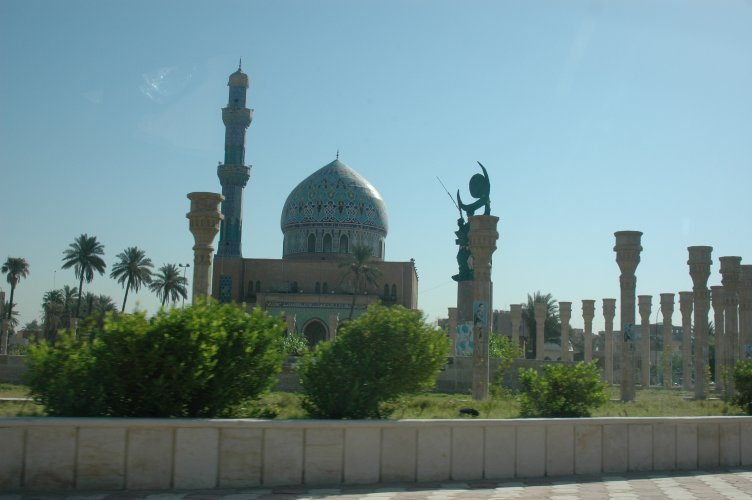 Mosque with a blue-tiled dome and tall minaret, surrounded by palm trees and ornate columns