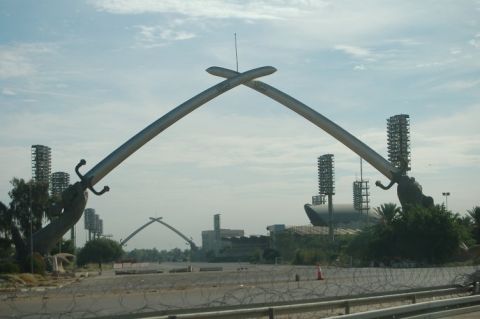 1996 Ford Bronco - The Victory Arch monument in Baghdad, Iraq, stands against a cloudy sky with stadium lights visible.