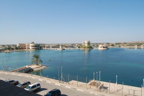 1996 Ford Bronco - Several cars are parked along a road next to a large body of water with buildings in the distance.