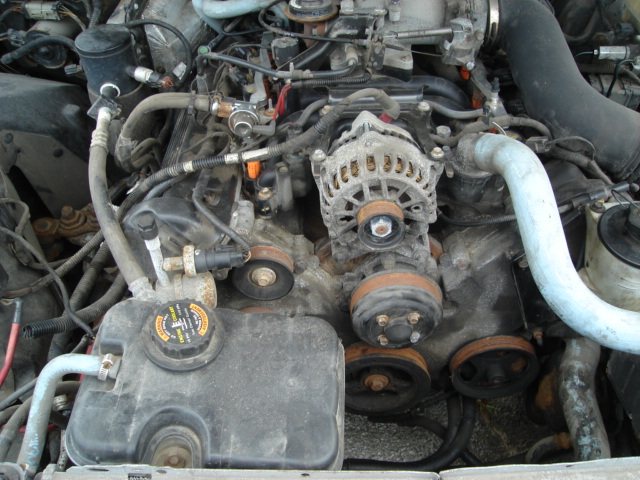 Engine bay with alternator, belts, and coolant reservoir visible. Some rust on pulleys