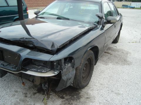 2000 Ford Crown Victoria - This dark sedan shows significant front-end damage, including a crumpled hood and missing headlight assembly.