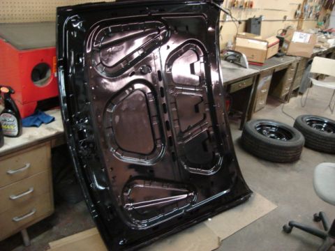 2000 Ford Crown Victoria - The underside of a black car hood is shown in a workshop setting, with spare tires nearby.