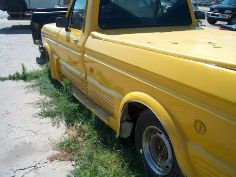 1979 Ford Bronco - A yellow pickup truck is parked on a cracked concrete surface next to overgrown grass.