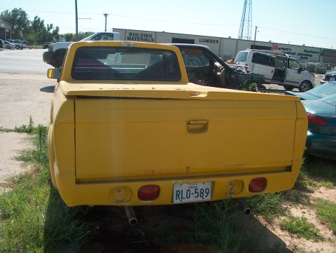 1979 Ford Bronco - A yellow pickup truck is parked in a lot with other vehicles and buildings in the background.