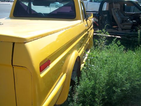 1979 Ford Bronco - The rear of a yellow pickup truck, possibly from 1979, is shown next to a dark green truck in a grassy area.