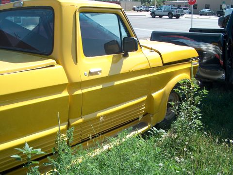 1979 Ford Bronco - Side view of a yellow 1979 Ford Bronco pickup truck parked next to another vehicle.
