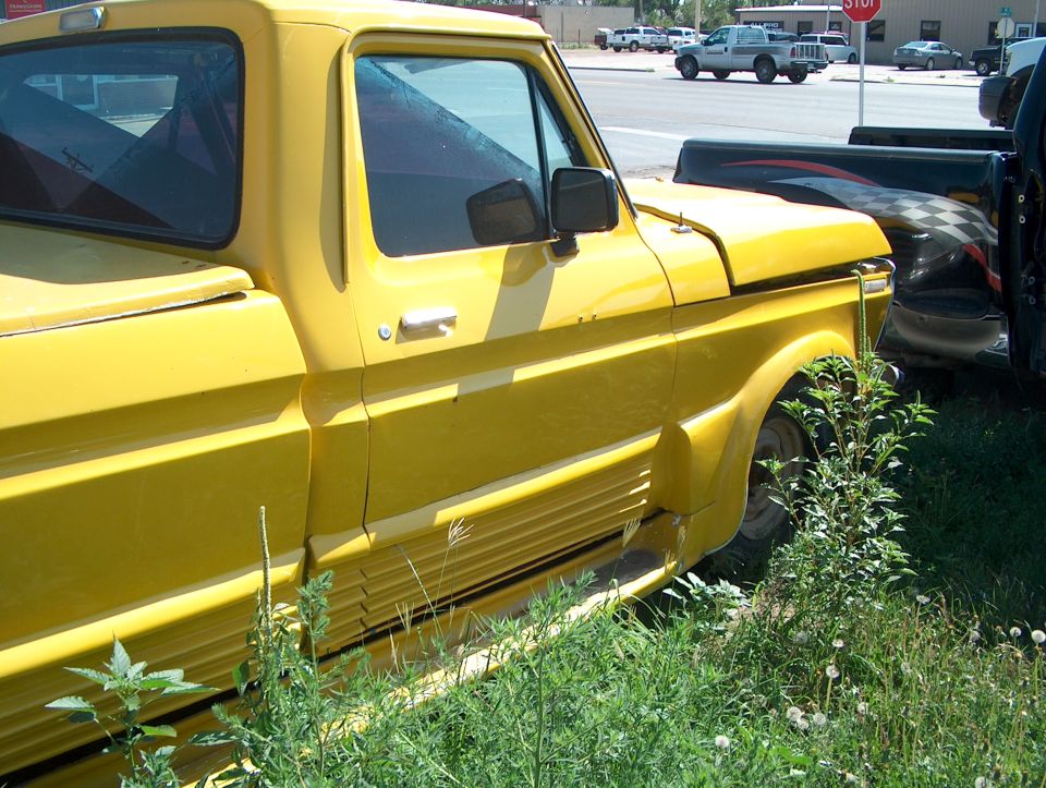Yellow 1979 Ford Bronco pickup truck side view, parked in grass