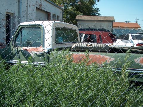 1979 Ford Bronco - A 1979 Ford Bronco sits behind a fence, partially obscured by weeds and other vehicles.