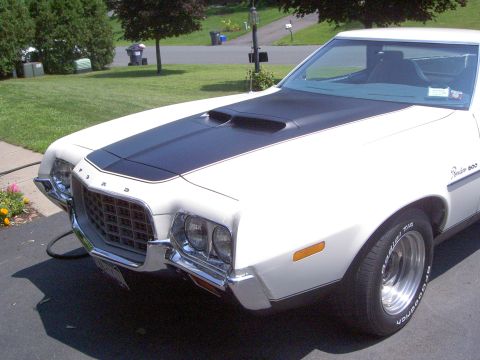 1972 Ford Ranchero - Tight driver-side front three-quarter view of a white Ford Ranchero 500 in a driveway, showing the flat-black hood stripe with twin hood sc…