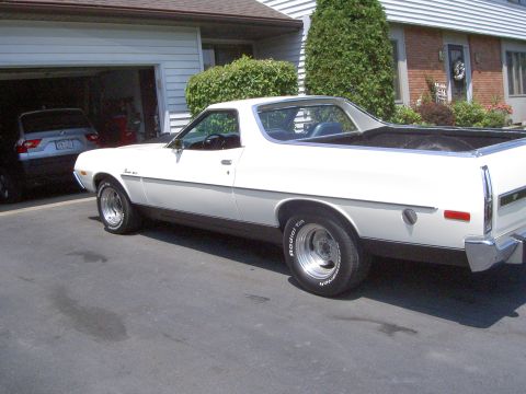 1972 Ford Ranchero - Three-quarter rear view from the driver's side of a white Ford Ranchero in a driveway, showing the open cargo bed, chrome rear bumper, side…