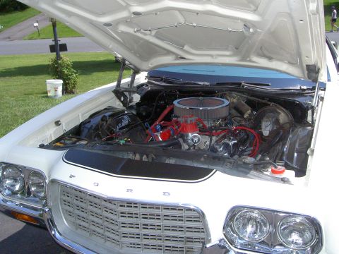 1972 Ford Ranchero - Open hood on a white Ford with the FORD-lettered grille and quad headlights in the foreground, revealing a V8 topped with a chrome-lid open…