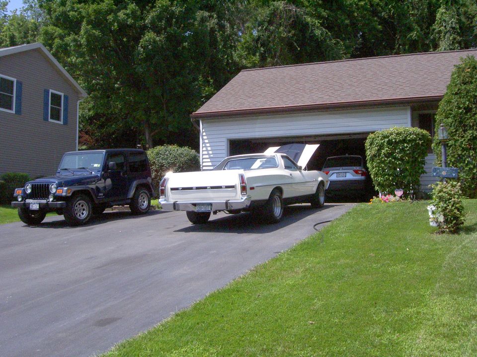 White Ford Ranchero with hood up in driveway beside a blue Jeep Wrangler