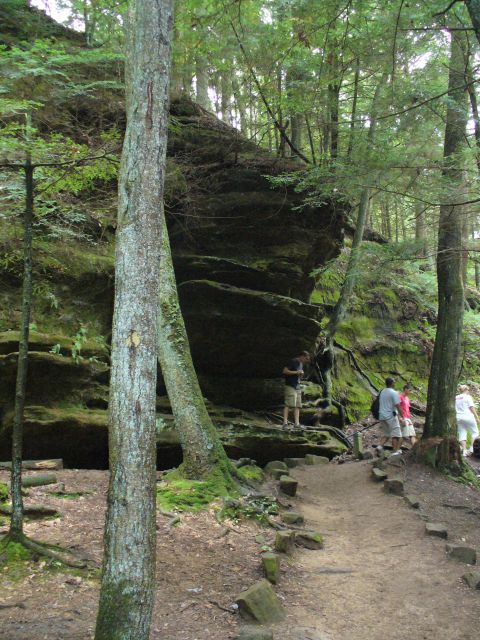 1991 Ford Probe - A group of people explore a wooded area with a prominent rock formation and a winding path.