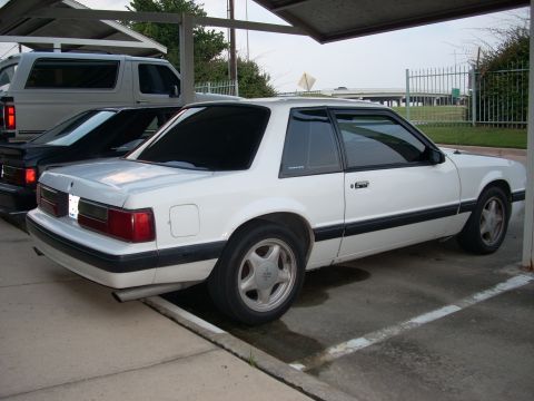 1991 Ford Mustang - A white 1991 Ford Mustang coupe is parked under a carport, viewed from the rear three-quarter angle.