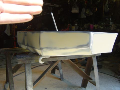 1989 Ford Bronco - A car bumper is being prepped for paint with body filler, resting on sawhorses in a workshop.