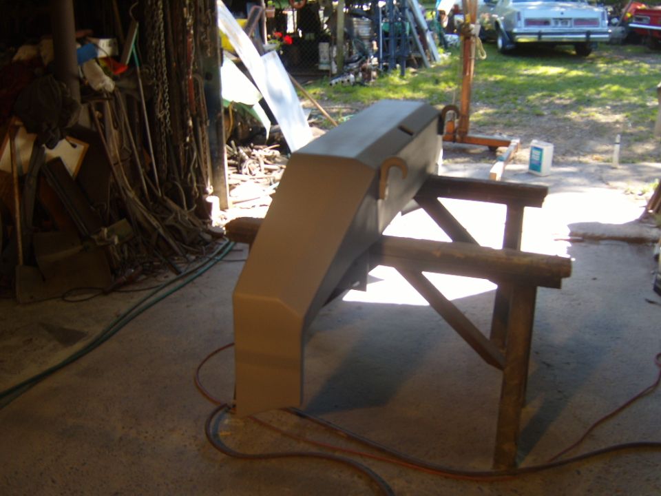 Ford Bronco front bumper on sawhorses, prepped for paint. Garage interior with tools and a car in the background