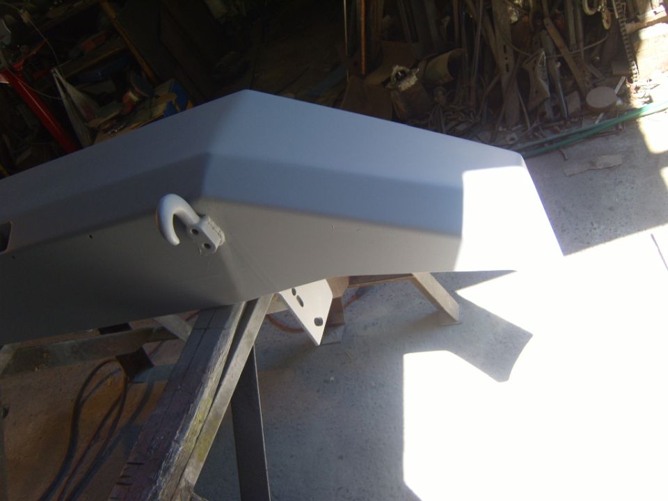 Gray primer front bumper with tow hook, supported by wooden sawhorses