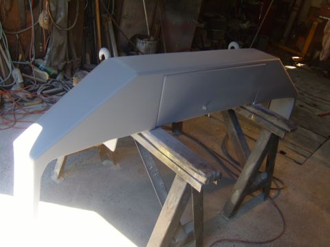 1989 Ford Bronco - Front bumper, likely for a truck or SUV, is prepped for paint and resting on sawhorses in a workshop.