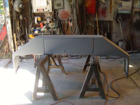 1989 Ford Bronco - A vehicle's front bumper, prepped for paint, sits on sawhorses in a cluttered garage.