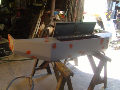 1989 Ford Bronco - Car bumper in primer with orange filler patches, supported by sawhorses in a workshop.