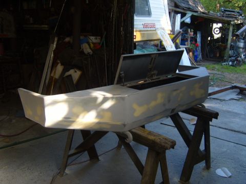 1989 Ford Bronco - A car bumper, prepped for paint, sits on sawhorses in a workshop setting.