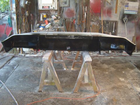 1989 Ford Bronco - A black front bumper is mounted on sawhorses in a workshop, ready for installation.