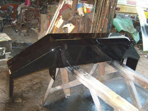 1989 Ford Bronco - A freshly painted black bumper rests on sawhorses in a workshop environment.