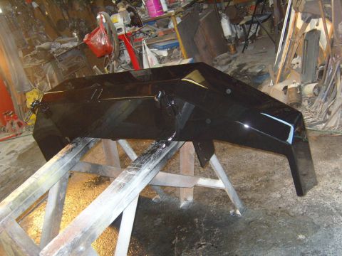 1989 Ford Bronco - A freshly painted black bumper rests on sawhorses in a cluttered garage setting.