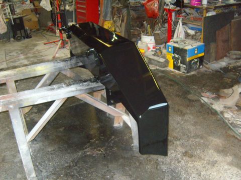 1989 Ford Bronco - A freshly painted black bumper is drying on sawhorses in a cluttered workshop.