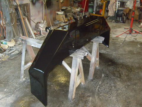 1989 Ford Bronco - A freshly painted black front bumper rests on sawhorses in a garage, awaiting reinstallation.