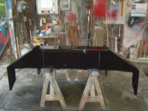 1989 Ford Bronco - A freshly painted black bumper sits on sawhorses in a cluttered garage, ready for installation.
