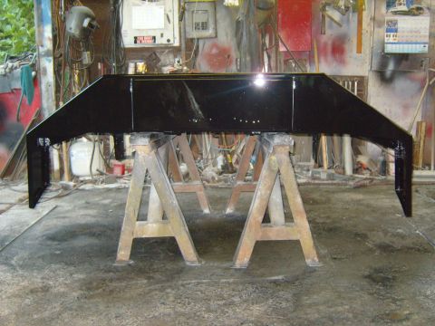 1989 Ford Bronco - A black bumper is mounted on sawhorses in a workshop, likely undergoing repairs or painting.