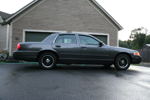 2000 Ford Crown Victoria - Side view of a dark gray sedan parked on a wet driveway in front of a house.