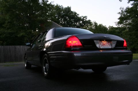 2000 Ford Crown Victoria - The rear of a dark 2000 Ford Crown Victoria sedan is visible with its taillights on.