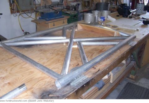 1977 Ford F-150 - A metal frame is assembled on a wooden workbench, with various tools and supplies visible in the workshop setting.