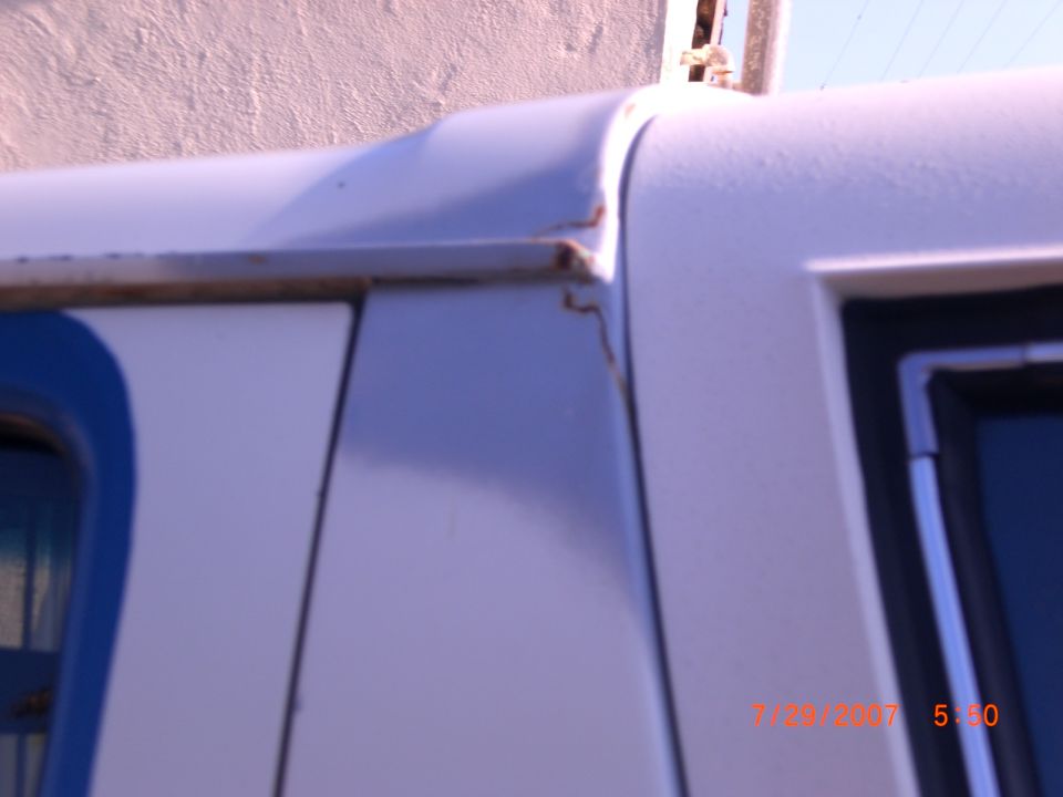 Close-up of white vehicle body panel with blue trim and rust spots near the roofline