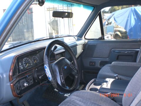 1991 Ford Bronco - The interior of a blue 1991 Ford Bronco shows cloth seats, a wood-trimmed dashboard, and a Ford steering wheel cover.