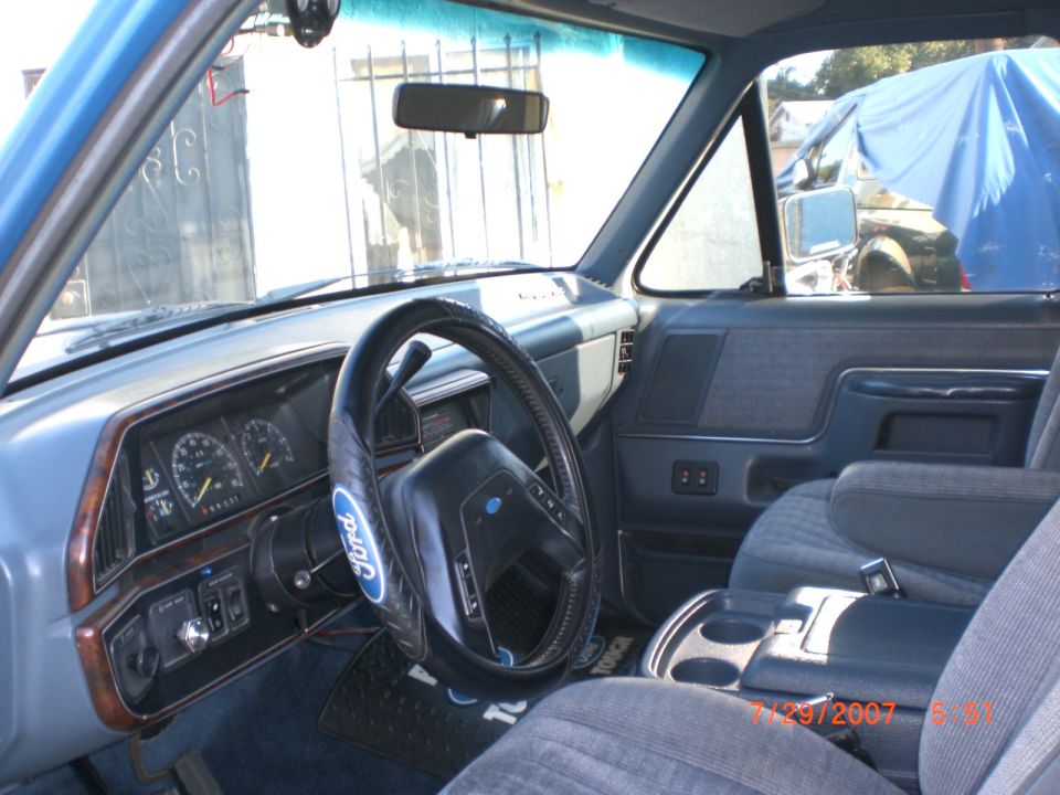Blue 1991 Ford Bronco interior with cloth seats, wood trim dashboard, and Ford steering wheel cover