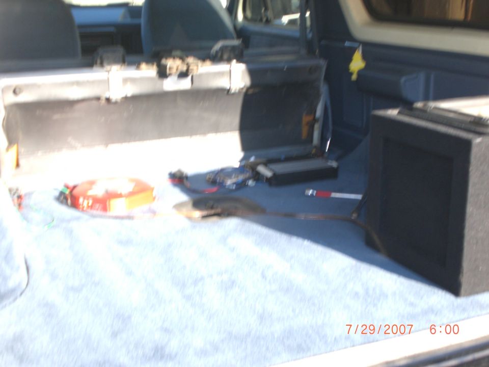 Interior cargo area of a vehicle with a blue towel on the floor, a subwoofer box, and various items including a red and yellow box