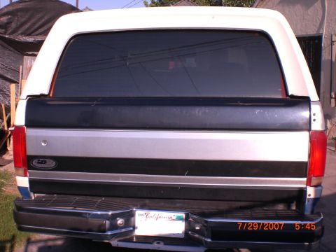 1991 Ford Bronco - The rear of a white Ford Bronco with a distinctive stripe pattern on the tailgate is visible.