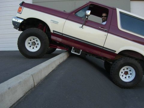 1991 Ford Bronco - A man drives a lifted Ford Bronco up onto a concrete curb.