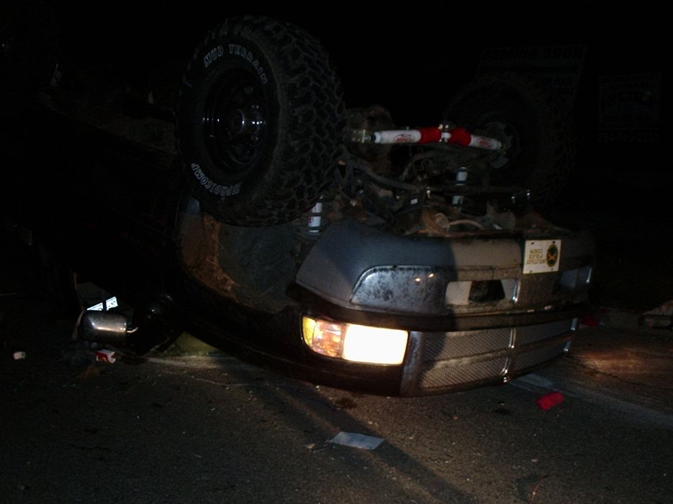 Overturned 1996 Ford Bronco, front view, showing damage and activated headlights