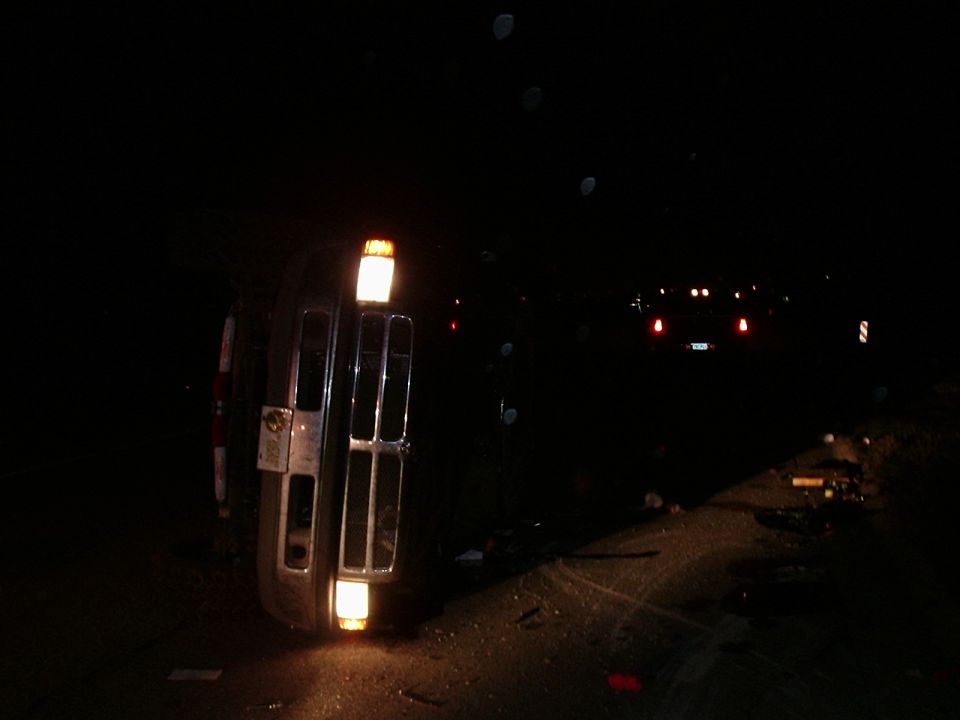 Overturned vehicle on its side at night, headlights on