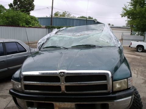 1996 Ford Bronco - A damaged dark green pickup truck sits outside, its windshield covered by plastic sheeting.