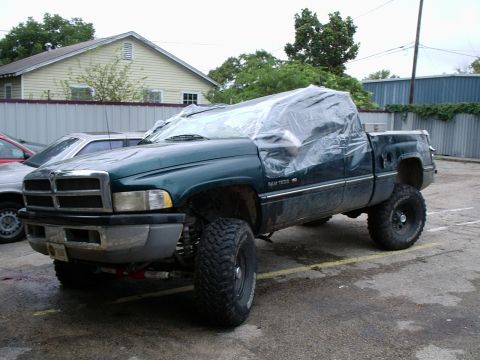 1996 Ford Bronco - Green lifted Dodge Ram 1500 V8 extended-cab pickup in a wet parking lot with its cab and windshield wrapped in clear plastic sheeting, fron…