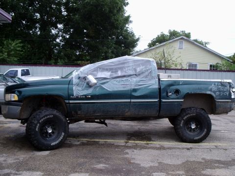 1996 Ford Bronco - A green Dodge Ram pickup truck with its cab covered in plastic, showing damage and handwritten text on the tailgate.