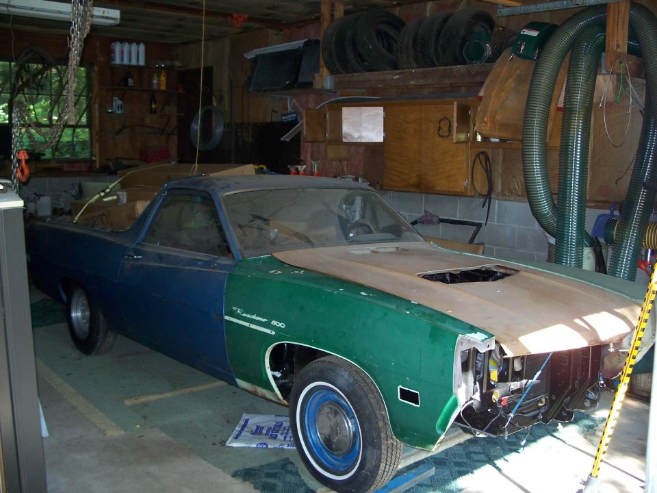 Blue and green Ford Ranchero in garage, hood removed, front end disassembled