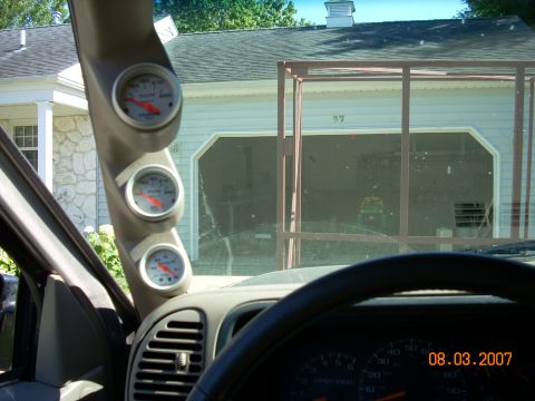 2000 Chevrolet Tahoe - A view from inside a vehicle shows an A-pillar mounted gauge cluster, with a garage and house visible through the windshield.
