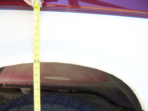1991 Ford Bronco - A measuring tape is held against the fender of a white vehicle, likely documenting lift kit measurements before or after installation.